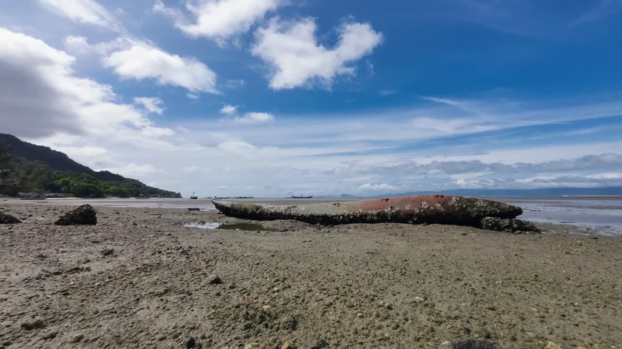 Timelapse footage of an old stranded kayak covered in seashells and algae on a sandy beach of Koh Phangan Thailand with moving clouds and scenic tropical seascape background