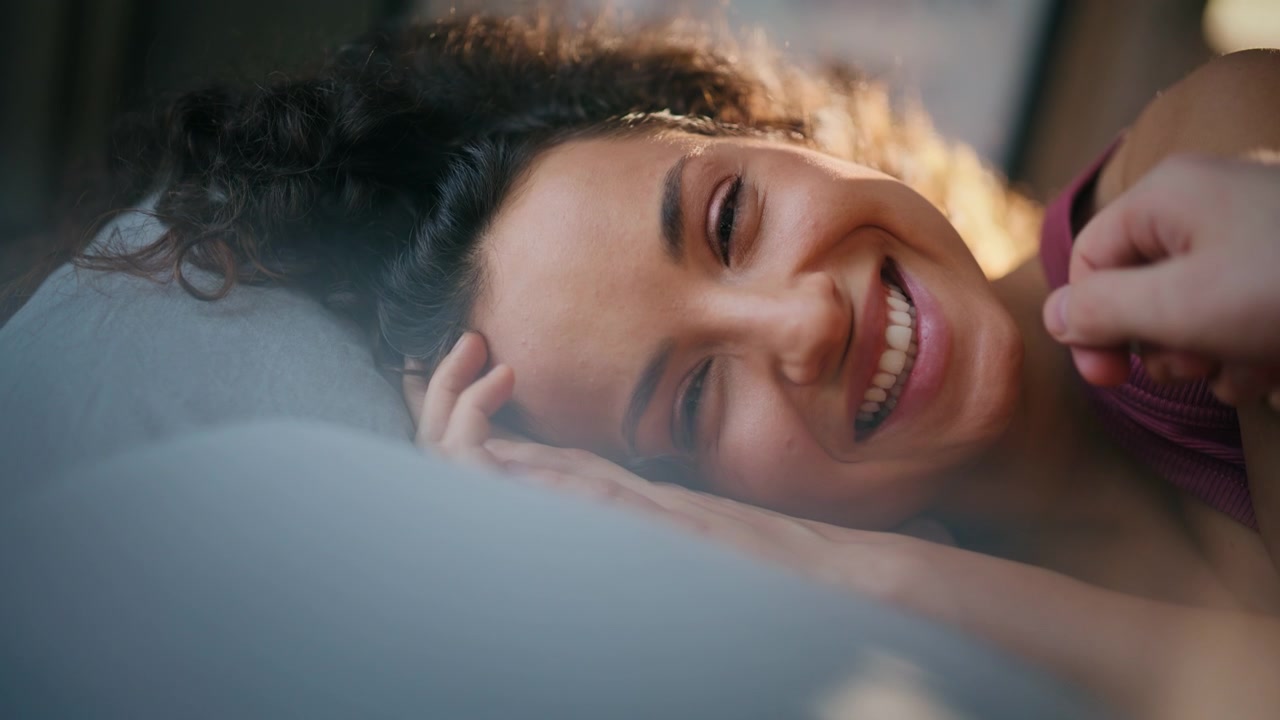 Close up smiling woman lying on pillow in morning light, man caressing face