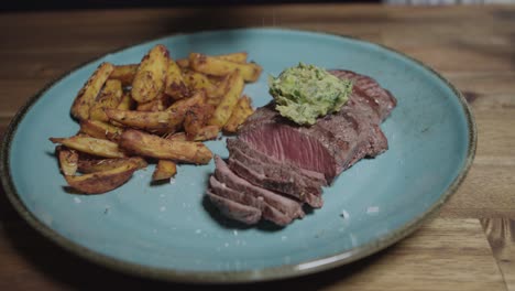 Chef-adds-salt-to-plate-of-meat-slices-with-cafe-paris-butter-and-french-fries