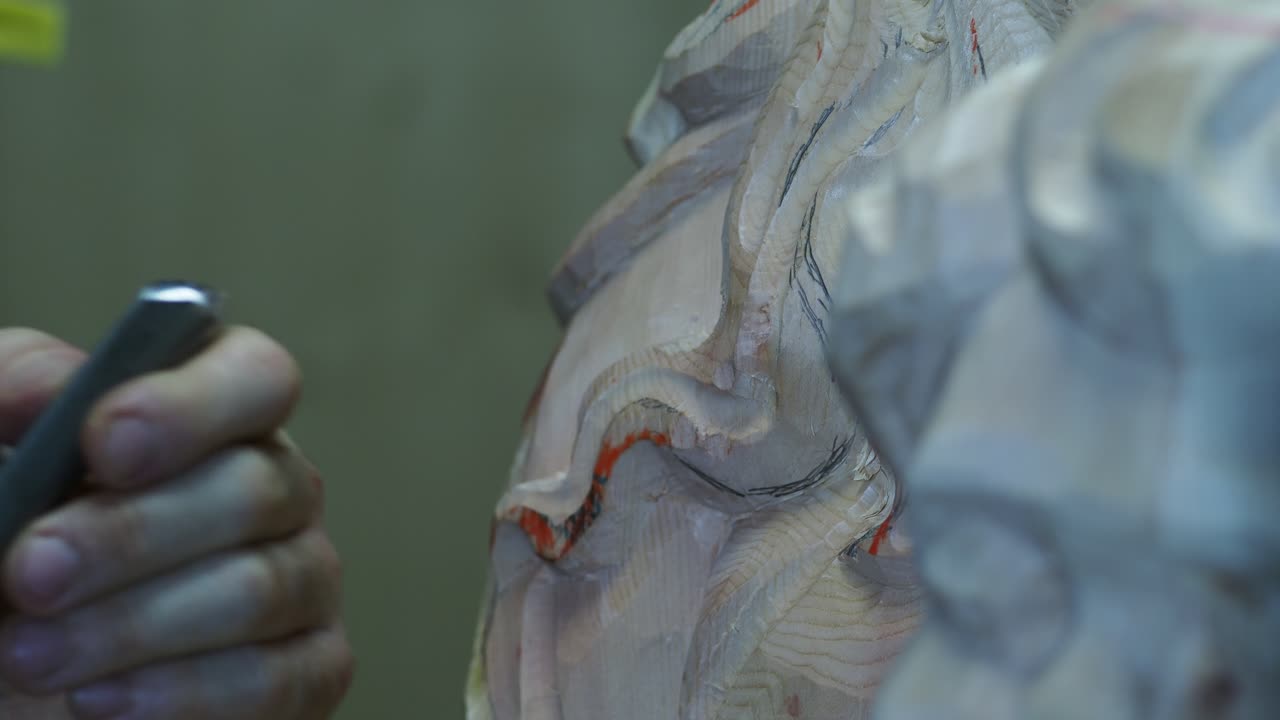 Extreme close-up of an artisan carving fine details into a wooden statue, showing precise hand movements with a chisel as the flowing hair of the figure takes shape
