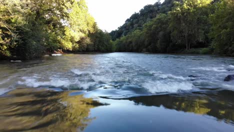 Die-Drohne-Fliegt-Rückwärts-Und-Tief-über-Einen-Fluss-Von-Rauem-Wasser-Zu-Glattem-Wasser