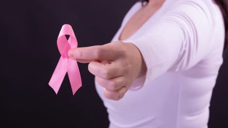 Video-of-midsection-of-caucasian-woman-holding-pink-cancer-awareness-ribbon,-on-black-background