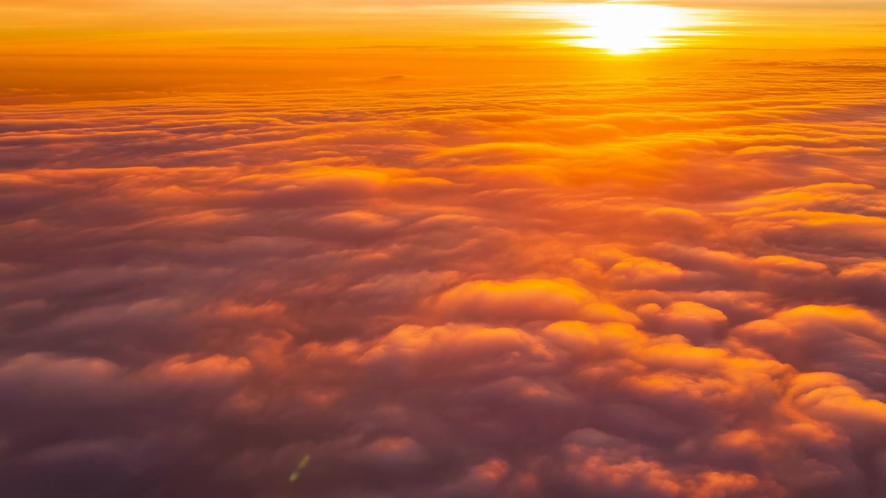 A breathtaking aerial view of a serene sunset over textured clouds, captured during a peaceful travel and nature relaxation period. The vibrant orange and yellow hues of the setting sun add.