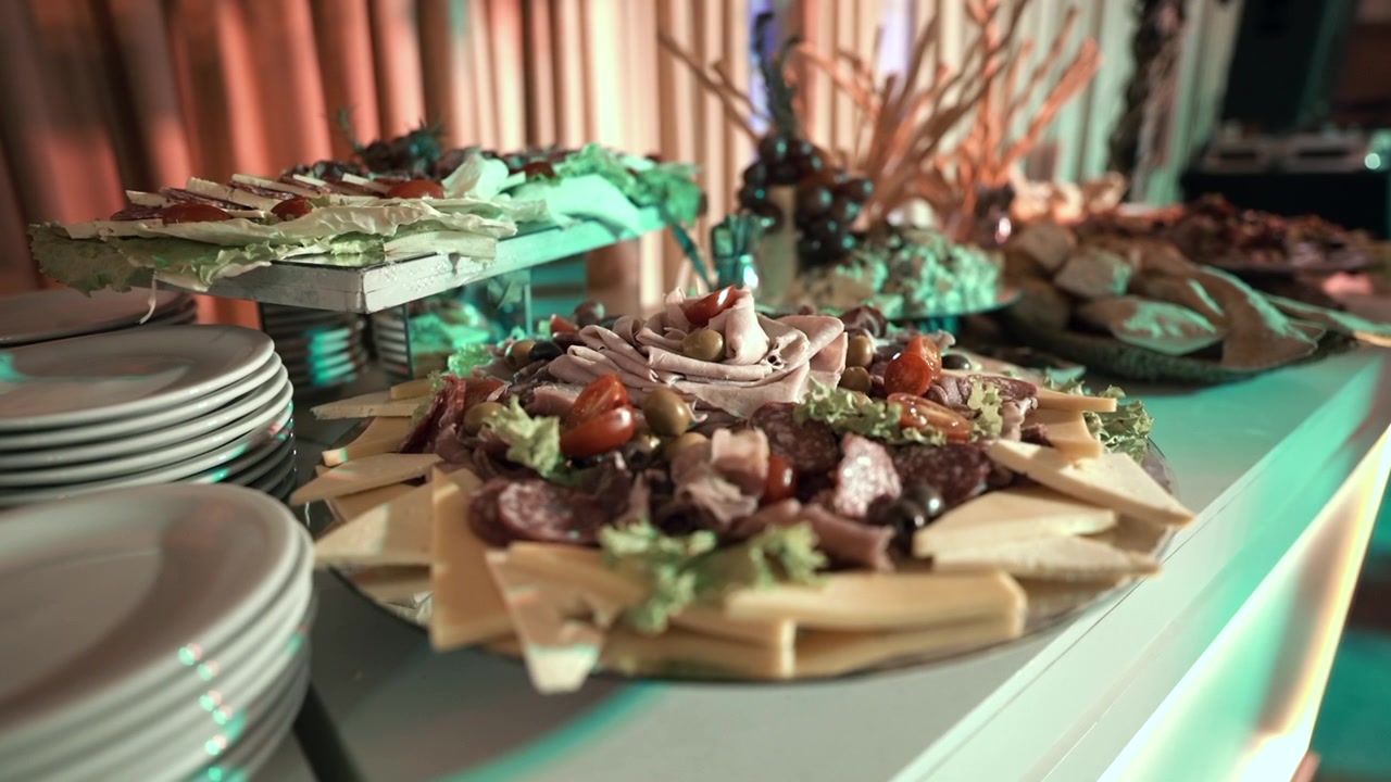 Un'abbondante esposizione di salumi e formaggi su un tavolo da buffet, accentuata da illuminazione ambientale. Perfetto per promozioni di catering o marketing di eventi di lusso.