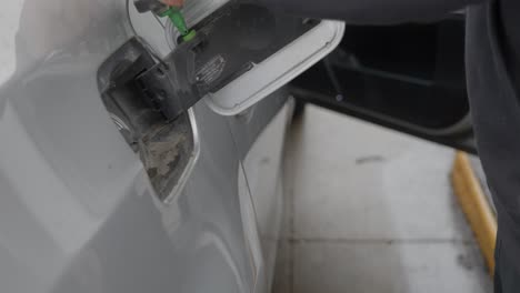 gas station white caucasian man with wedding ring filling up silver car with opened fuel tank cover and twisting off and storing gas cap then turning to pump