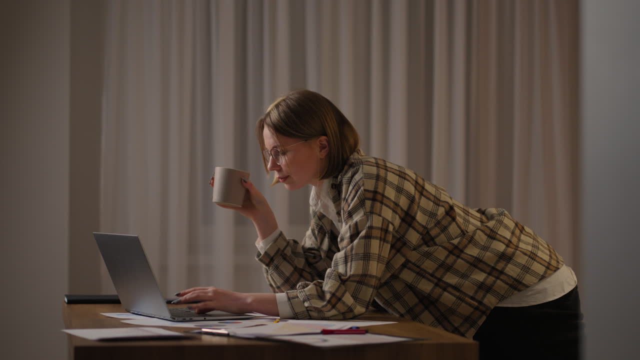 A girl works from home or a student is studying from home or a freelancer. She uses a laptop and a phone. girl sit at desk in living room study on laptop making notes concentrated young woman work