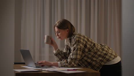una chica trabaja desde casa o un estudiante está estudiando desde casa o un freelancer. ella usa una computadora portátil y un teléfono. la chica se sienta en el escritorio en la sala de estar estudia en la computadora portátil tomando notas concentrada mujer joven trabaja