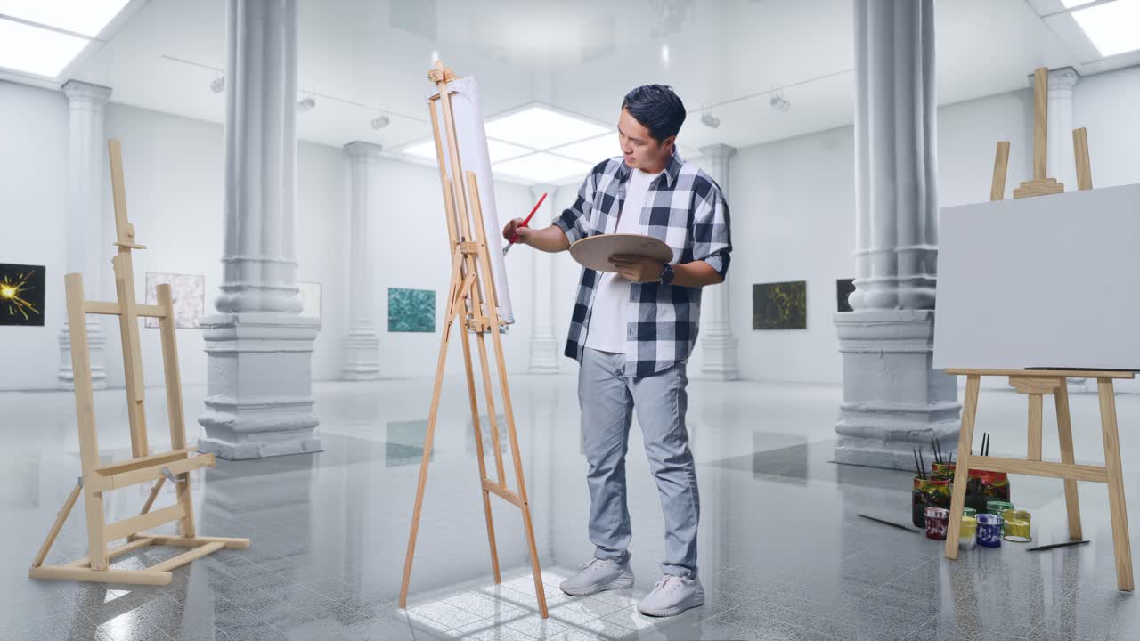 Un artista maschio asiatico a figura intera è concentrato a dipingere su tela con colori a olio e pennello in una galleria.