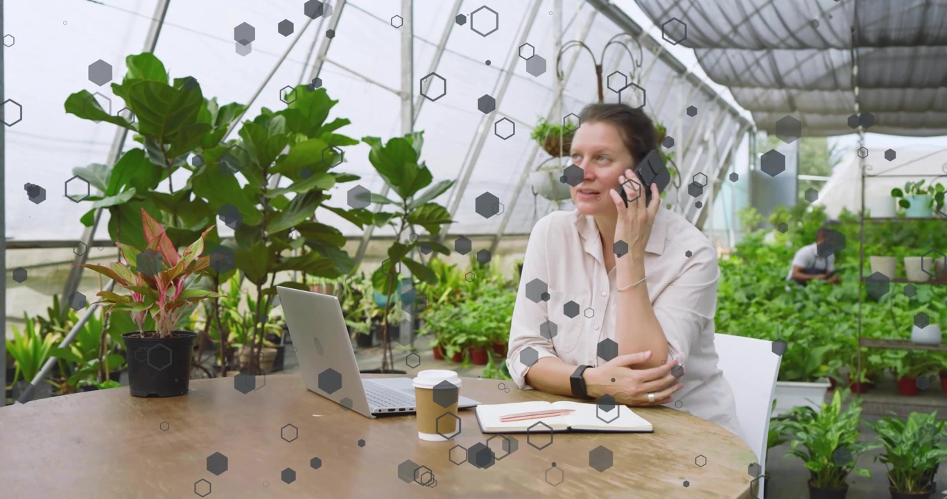 Mujer abriendo un cuaderno en un invernadero, registrando investigación de plantas y luego llamando a un proveedor desde su teléfono.