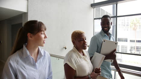 walking in office, diverse colleagues discussing work while holding documents and laptop