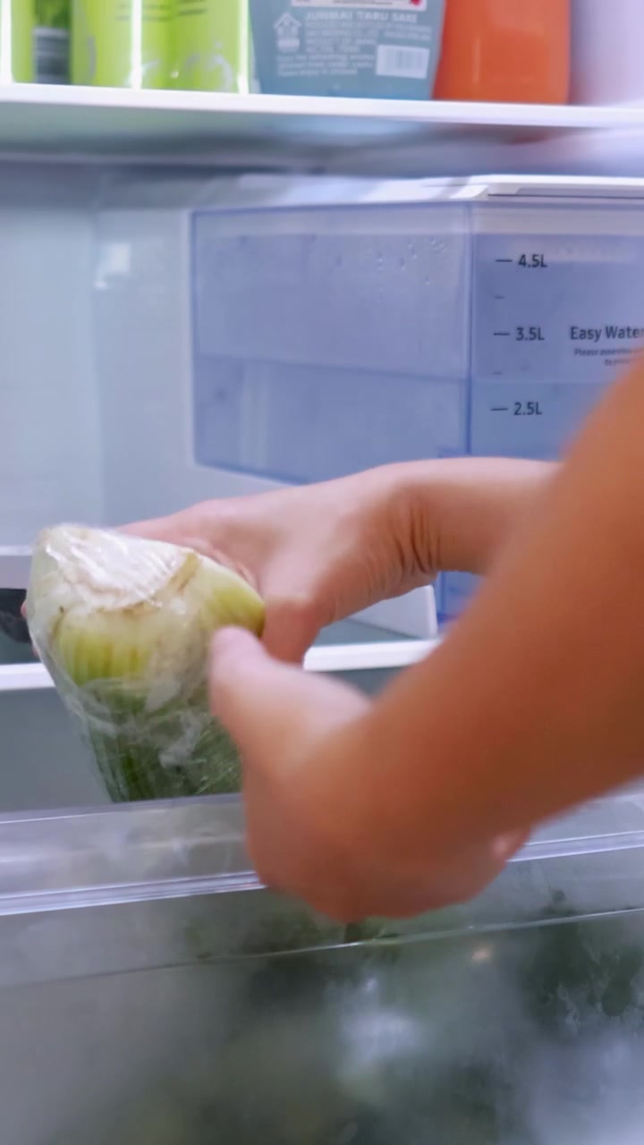 Una persona apre un frigorifero e prende verdure fresche, evidenziando un ambiente di cucina domestica.