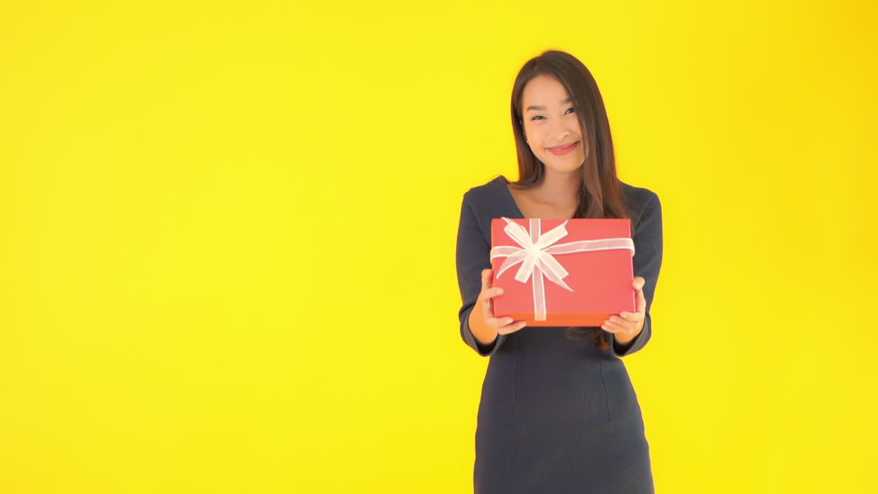 Packed Gift Box Presented by Attractive Asian Female, Isolated on Yellow Screen Background