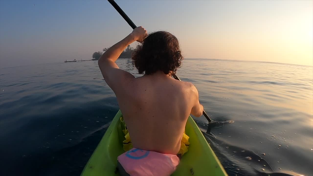 joven remando en un kayak en el océano con una isla como fondo