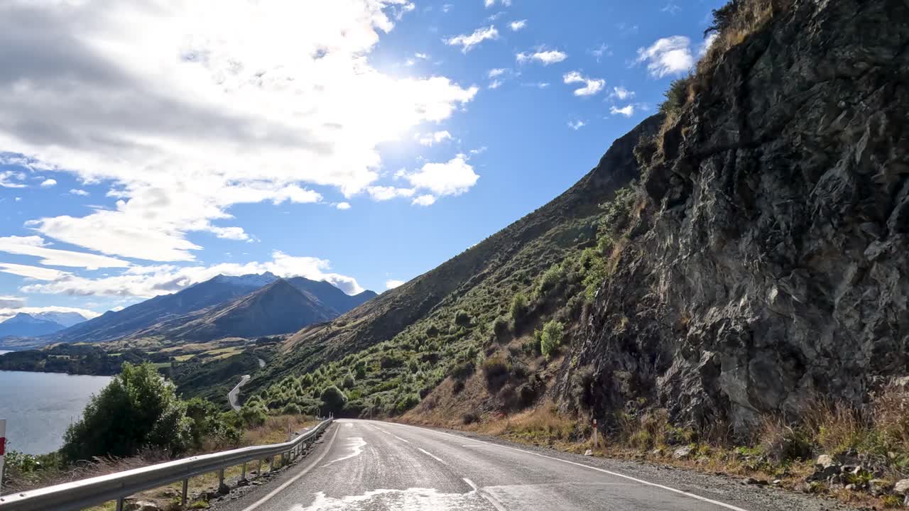 A 30-second drive through Queenstown's mountainous landscape, featuring a winding road beside a serene lake under bright daylight