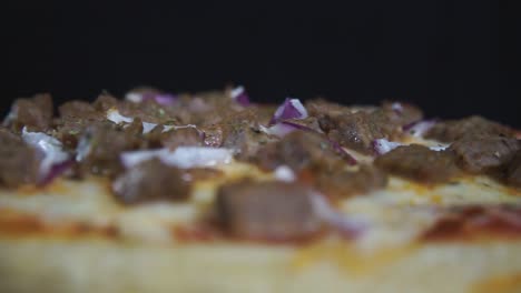 pizza cocida con cebolla, ternera y queso girando frente al fondo negro, de cerca