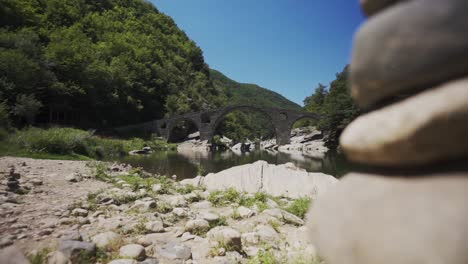 A-view-from-a-distance-of-the-historical-Devil's-Bridge-and-the-Arda-River,-at-the-foot-of-Rhodope-Mountains,-in-Ardino,-Bulgaria