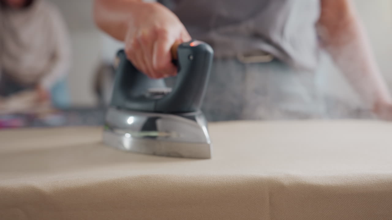Cloth stylist moving pressing iron on cotton material, placing it on protective pad, focusing on precise heat application, ensuring crisp finish, controlling steam for polished garment