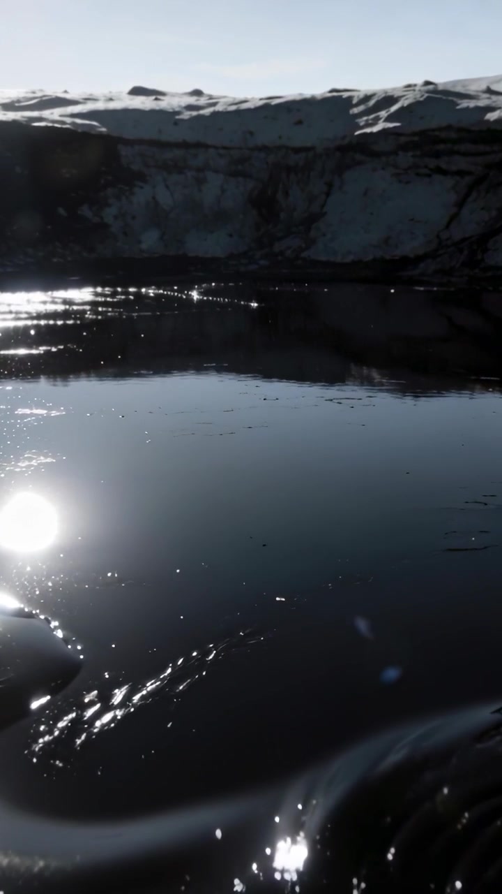 Vertical video: Shifting water with eddy making ripples at snowy ridge, sun glint causing motion