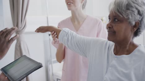 diverse male doctor with tablet and happy female physio treating senior female patient, slow motion
