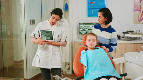 Doctor-holding-tablet-with-x-ray-showing-it-to-mother-of-girl-patient