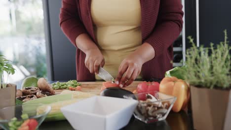 midsection of african american plus size woman chopping vegetables in kitchen, slow motion