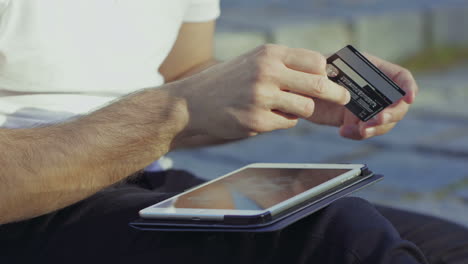 foto recortada de um jovem a digitar o número do cartão no tablet.