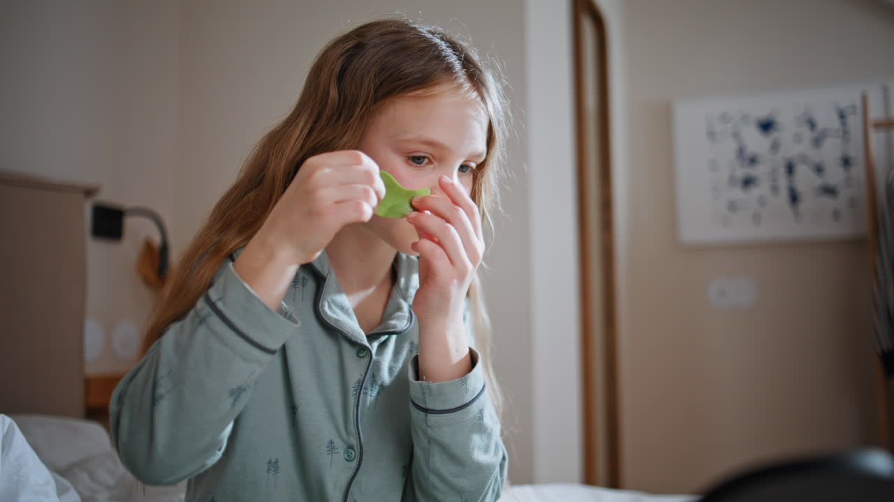 Bambino che si mette i patch sotto gli occhi e si rilassa in camera da letto, primo piano. Trattamenti di bellezza per bambini