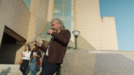 businessman drinking coffee and using phone outside an office building