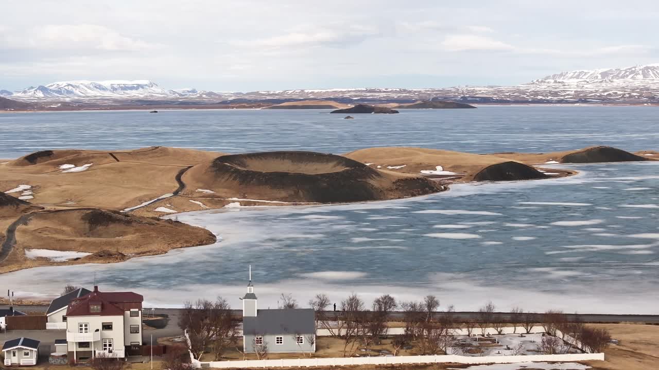 aerial of Reykjahlíð church facing frozen Mývatn lake and volcanic craters near Skútustaðir Iceland