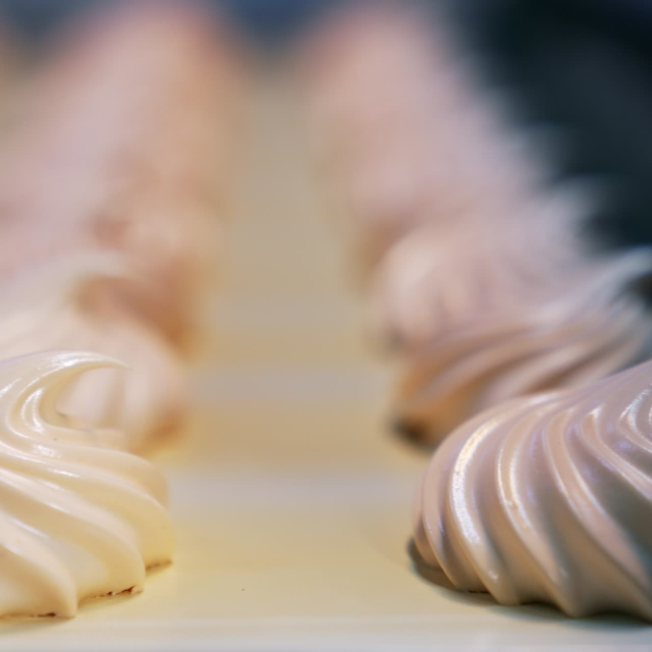 Manufacturing white zephyr candies at modern confectionery factory. Creamy sweets moving along the conveyor. Close up. Blurred backdrop