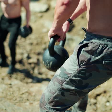 Bodybuilders training among nature. Heavy kettlebell in man's arms during workout. Athletic men lifting weights. Close-up.