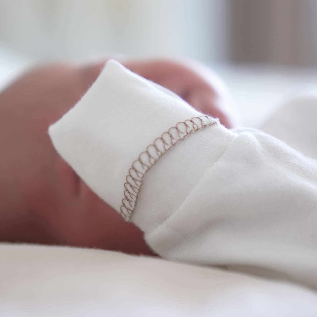 Baby in a light blouse wakes up and grimaces. Close up newborn baby in white clothes