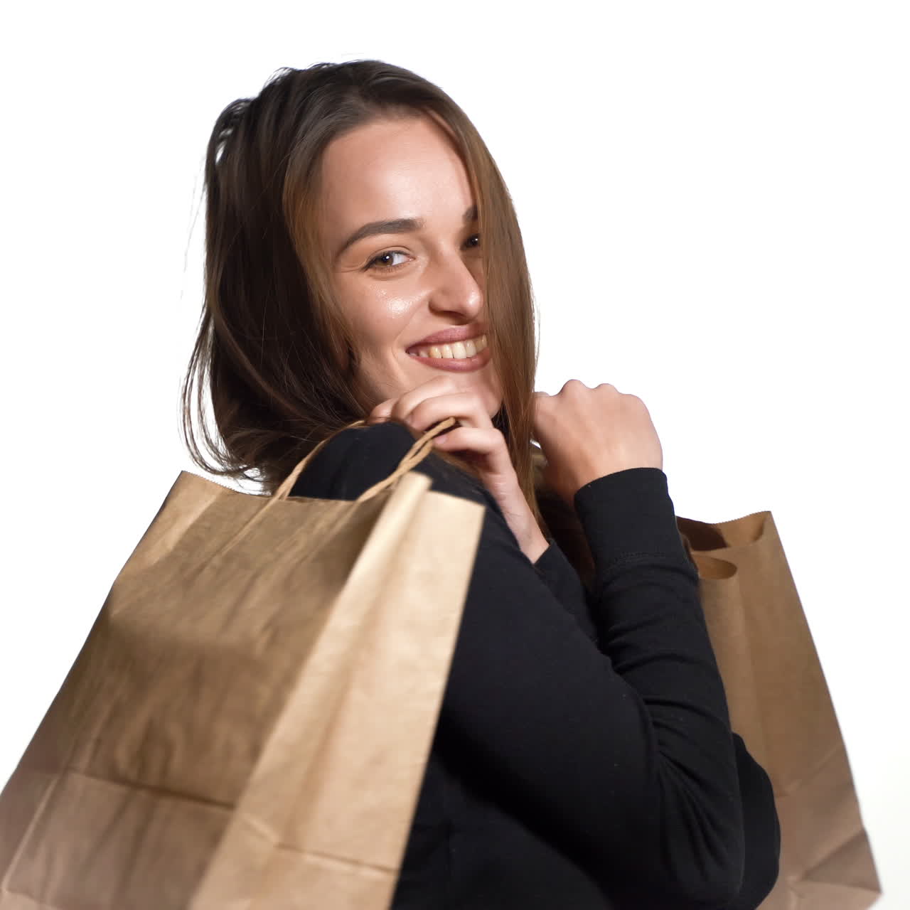 A beautiful woman in a black jumper is holding brown packages in her hands and posing with them after shopping on a white background.