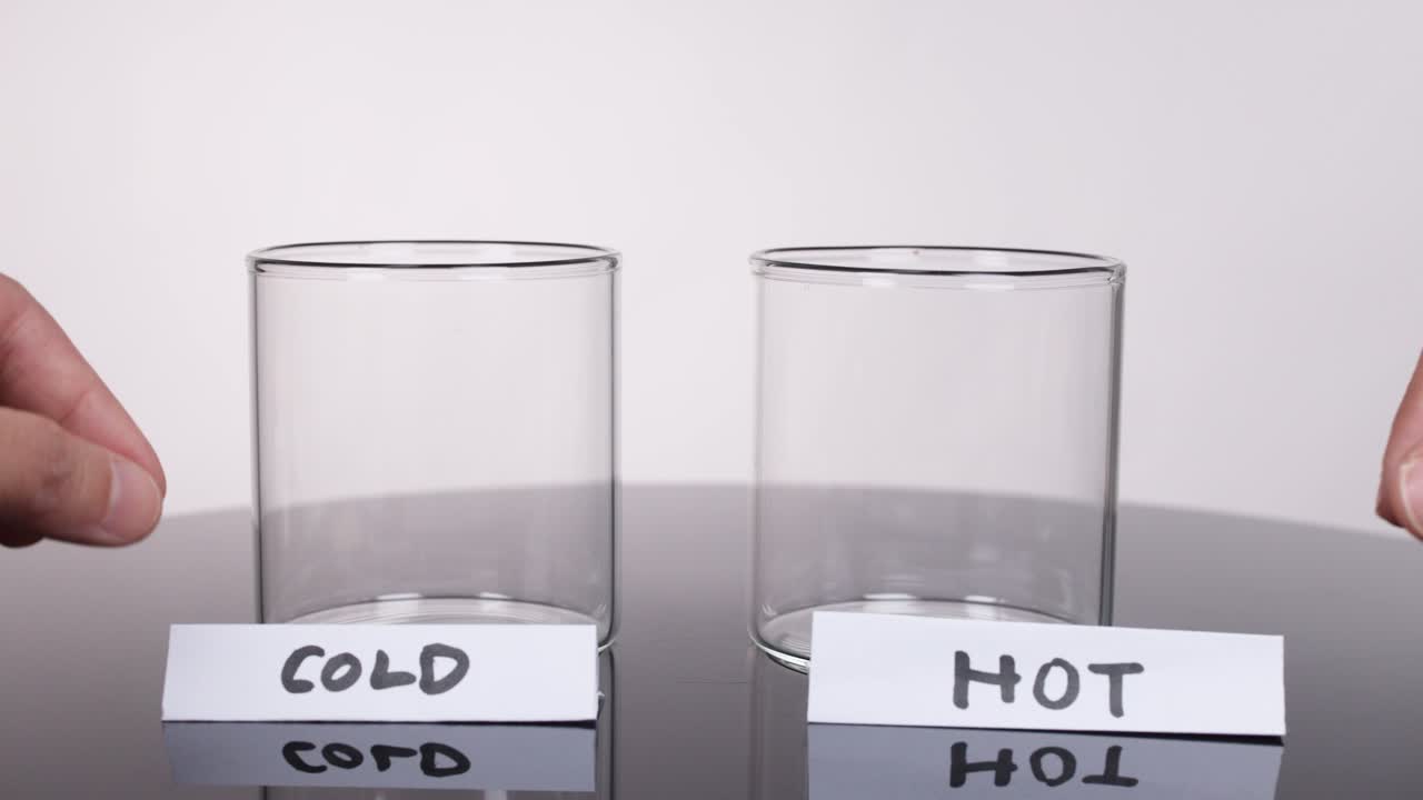 Hands label two empty glass cups "cold" and "hot" in a bright science setup