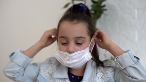 portrait of little girl looks upset at camera, child wears protective medical mask on his face against infection covid virus, during pandemic epidemic of disease, close up