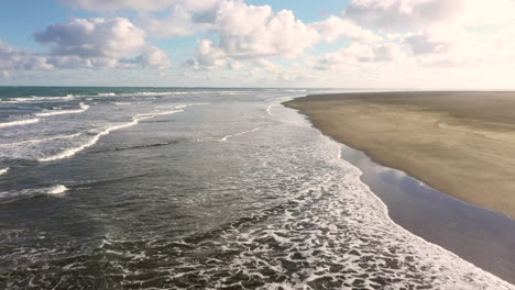 Flying-above-black-sandy-Whatipu-beach-and-waves-in-Huia-Reserve,-New-Zealand