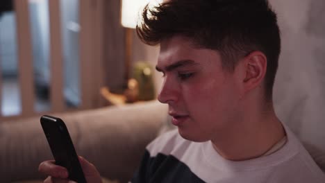 Young-man-looking-at-a-smart-phone-on-the-sofa-at-a-cosy-home