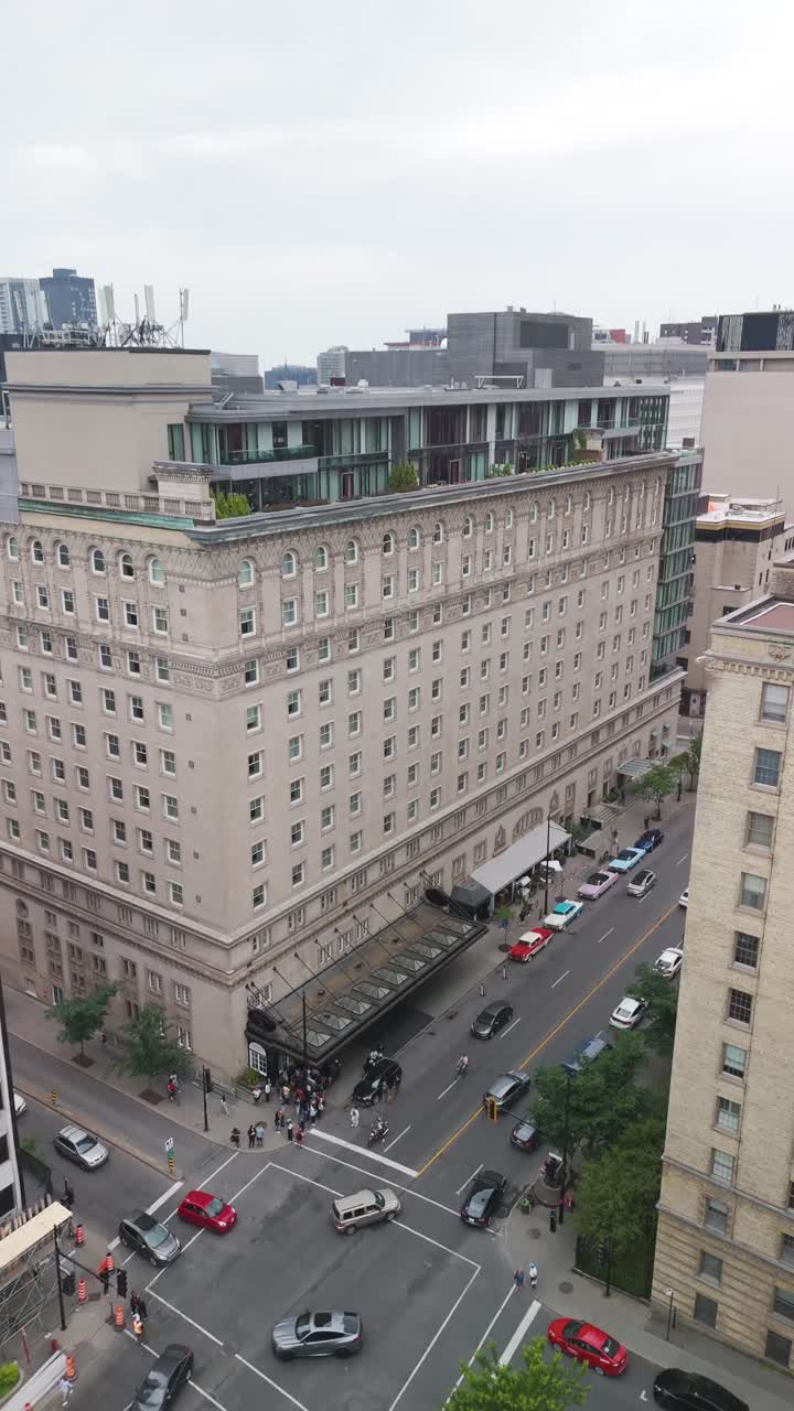 Top-down aerial drone shot of a historic luxury hotel in downtown area. Classic architecture with a striking modern rooftop addition, surrounded by dense urban scenery. Vertical shot 9:16.