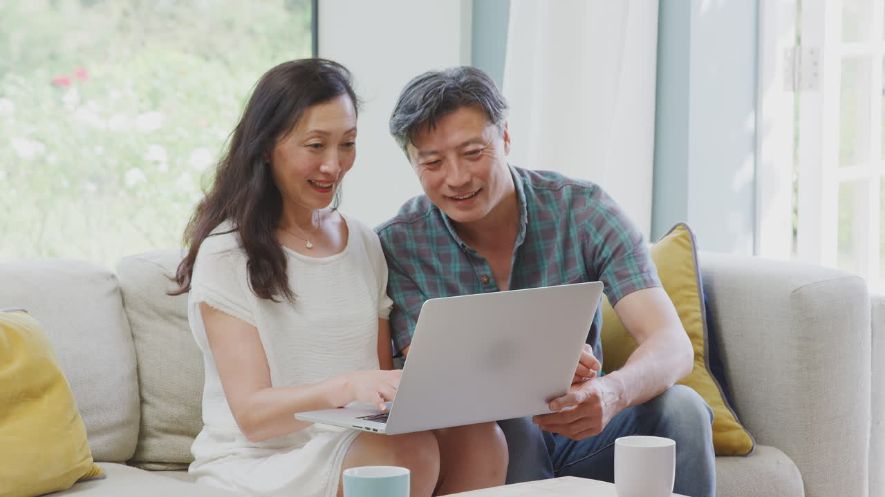 Mature Couple Sitting On Sofa At Home Making Video Call On Laptop