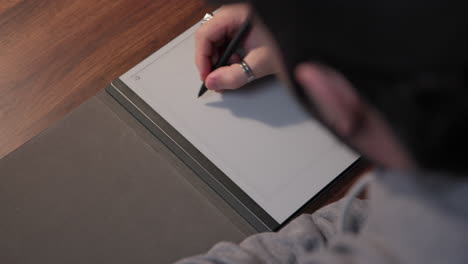 a young man writing on a digital tablet, over the shoulder