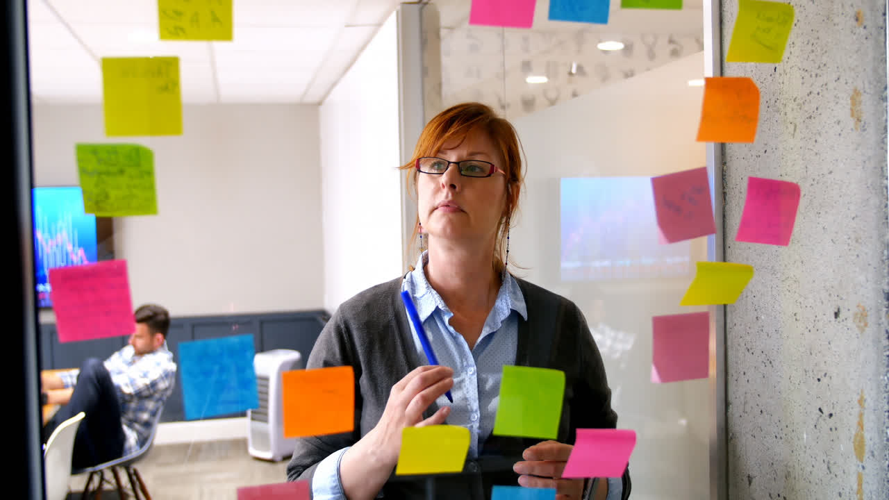 Female executive looking on sticky note on glass wall 4k