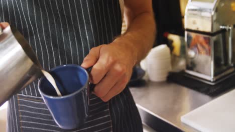 camarero masculino vertiendo leche en una taza en el café 4k