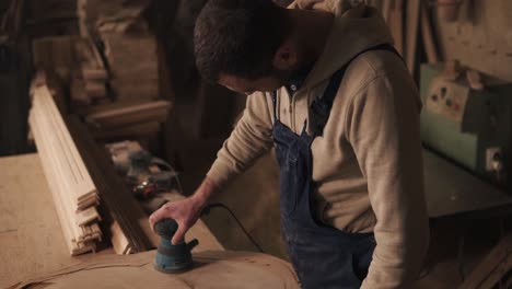 el carpintero termina de moler la pieza de madera, apaga la amoladora y comprueba si la superficie está rugosa