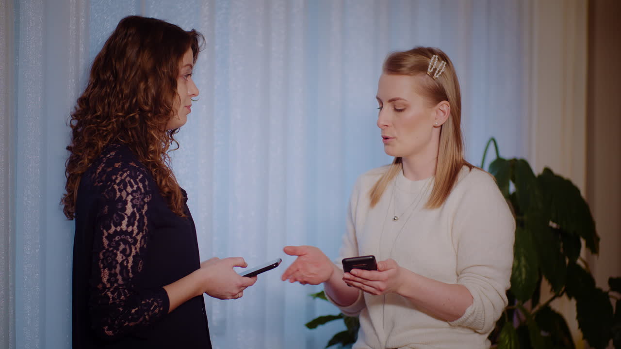 Two women talking and using smartphones indoors