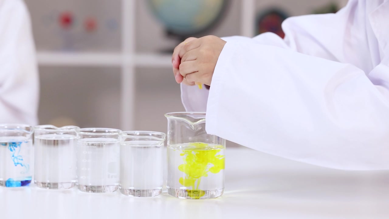 Primo piano di uno studente che aggiunge colorante giallo all'acqua in un laboratorio scientifico scolastico.