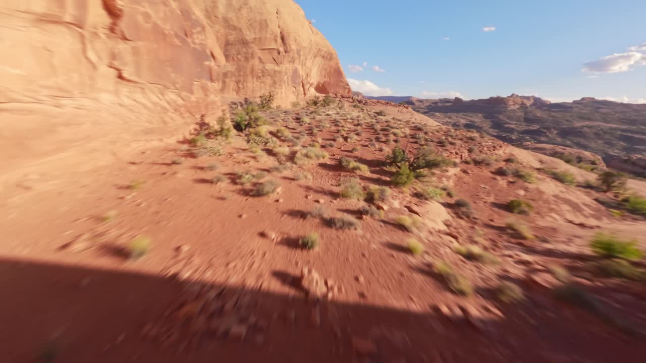 An FPV drone diving towards and flying through the red sandstone Funnel Arch in the sandy and rocky desert of Moab Utah while in close proximity to nearby rocks