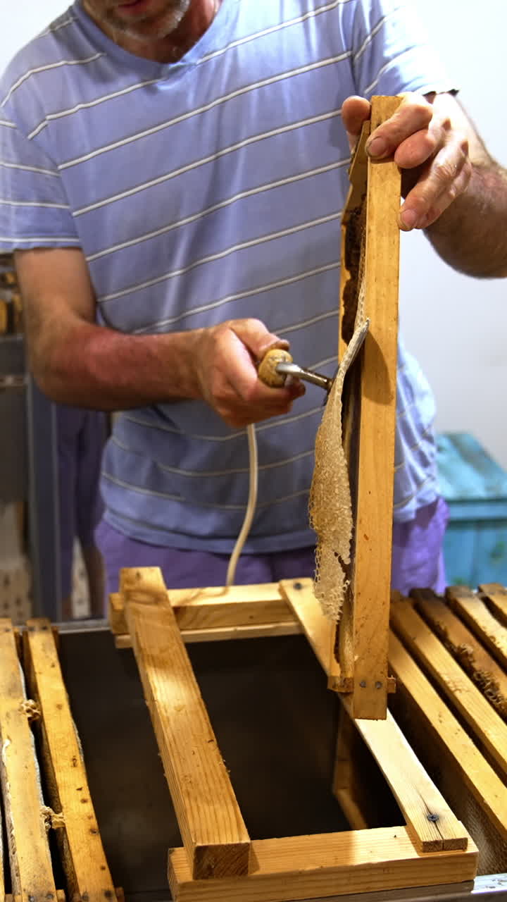 Beekeeper holding a frame and peels off the covers from the sealed cells. Preparation of frames for extracting honey. Vertical video