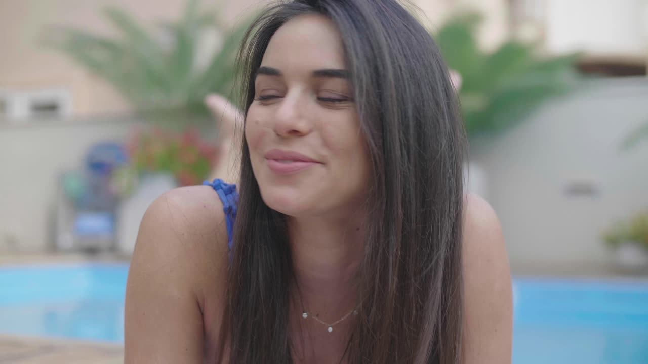 alegre y atractiva mujer morena tomando el sol junto a la piscina en un hotel de lujo