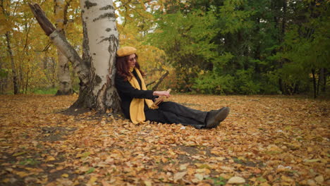 student in yellow beret relaxes by reading under autumn trees, surrounded by a carpet of dry leaves, embodying the serene atmosphere of fall