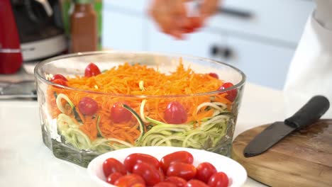 añadiendo tomates en rodajas a un tazón de zanahorias trituradas y fideos de calabacín en espiral zoodles añadiendo a un tazón un estilo de vida vegetariano saludable dieta de desintoxicación